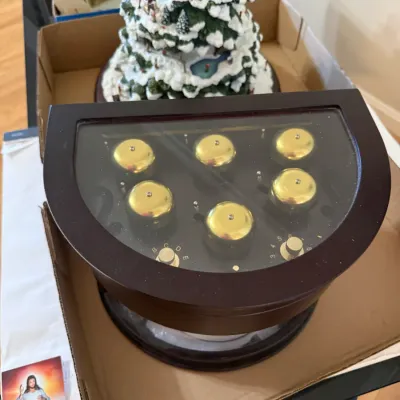 Sale Photo Thumbnail #353: Wooden Mr. Christmas Symphonium musical display box featuring six brass bells visible beneath a glass top panel, shown alongside a snowy Christmas village tree display.