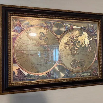 Sale Photo Thumbnail #90: Framed gold foil world map reproduction featuring double-hemisphere cartography, celestial insets, and ornate classical illustrations in an ornate dark wood frame.
