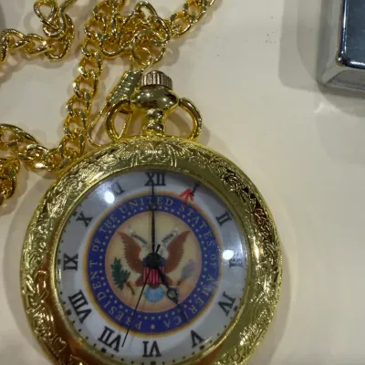 Sale Photo Thumbnail #420: Gold-tone pocket watch with chain featuring the Seal of the President of the United States on the dial.