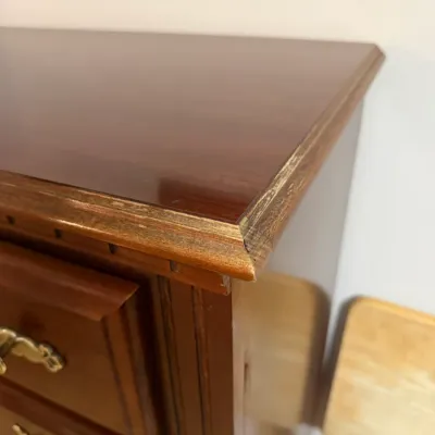 Sale Photo Thumbnail #130: Close-up of a vintage cherry wood dresser featuring brass bail handles and edge wear along the top surface.
