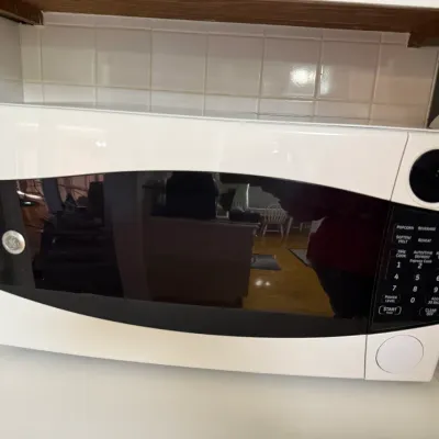Sale Photo Thumbnail #161: White GE countertop microwave with a dark tinted door and digital keypad control panel.