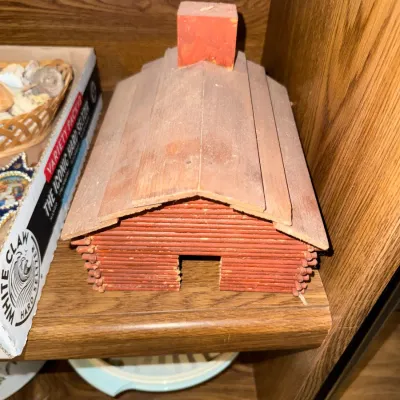 Sale Photo Thumbnail #285: Handcrafted vintage miniature log cabin constructed from matchsticks or small dowels, featuring a red painted chimney and finish.