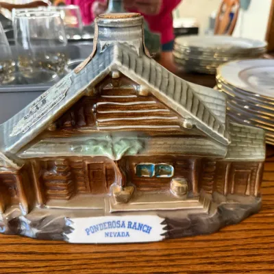 Sale Photo Thumbnail #326: Vintage ceramic decanter shaped like a log cabin, featuring 'Ponderosa Ranch Nevada' printed on the front base.