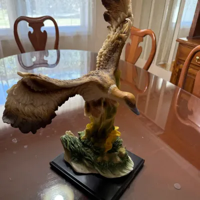 Sale Photo Thumbnail #262: Painted resin figurine depicting a waterfowl bird in flight, mounted on a dark wooden display base.
