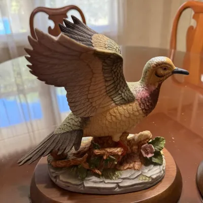 Sale Photo Thumbnail #235: Hand-painted porcelain ring-necked pheasant figurine depicting a bird in flight, mounted on an oval wooden base with a brass nameplate.