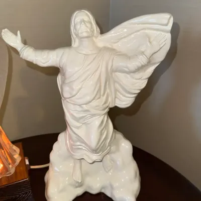 Sale Photo Thumbnail #231: Vintage white glazed ceramic statue of Jesus Christ depicted ascending on clouds with outstretched arms.
