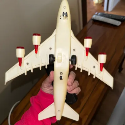 Sale Photo Thumbnail #324: Vintage off-white plastic toy airplane showing bottom view with landing wheels, four engine pods, red-tipped detailing, and attached cord handle.