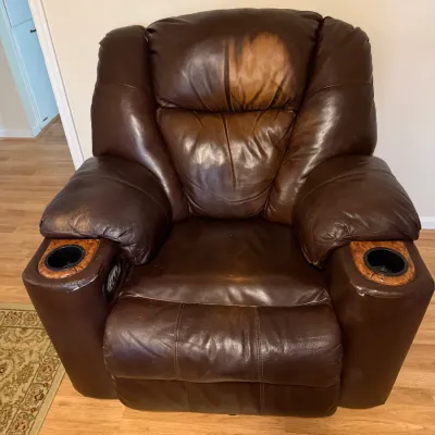 Sale Photo Thumbnail #120: Brown leather home theater power recliner with built-in cup holders, wood-grain accents, and visible wear on the headrest.
