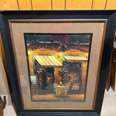 Sale Photo Thumbnail #397: Framed art print depicting a French crêperie and restaurant scene, set in a wide brown mat and dark wood frame with gold inner trim.