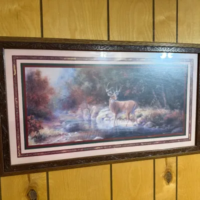 Sale Photo Thumbnail #398: Framed wildlife art print depicting a white-tailed buck standing in a forest stream, housed in an ornate carved wooden frame with double matting.