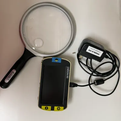 Sale Photo Thumbnail #154: Pebble HD portable electronic magnifier with power supply charger alongside a large traditional handheld magnifying glass.