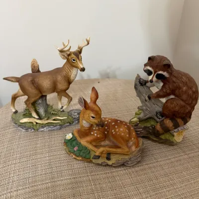 Sale Photo Thumbnail #340: Trio of painted resin woodland wildlife figurines, including a standing buck, a resting spotted fawn, and a raccoon on a log.