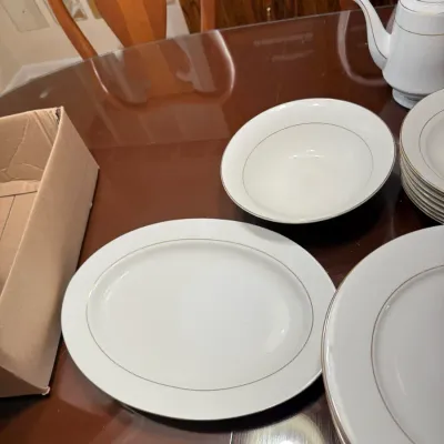 Sale Photo Thumbnail #303: White porcelain dinnerware set featuring fine gold trim lines, including an oval platter, bowls, dinner plates, and a teapot.