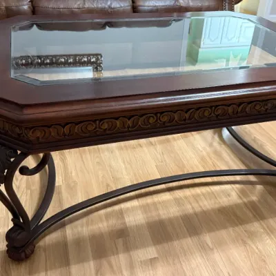 Sale Photo Thumbnail #28: Traditional wooden coffee table featuring a glass insert top, carved relief apron, and wrought iron scrollwork legs with a stretcher base.