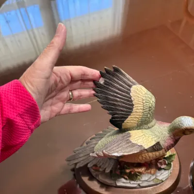 Sale Photo Thumbnail #238: Hand-painted porcelain bird figurine on a wooden base, depicting a bird in flight with noticeable damage to the wing tip.