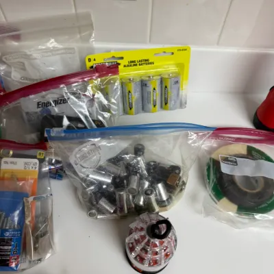 Sale Photo Thumbnail #164: Assortment of household hardware supplies, including plastic bags filled with loose batteries, a new four-pack of Performax D batteries, rolls of tape, and small hardware fasteners.