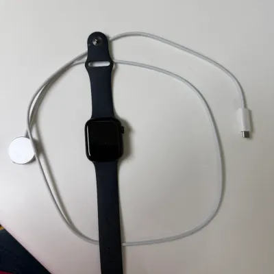 Sale Photo Thumbnail #151: Black Apple Watch with dark sports band and white magnetic USB-C charging cable.