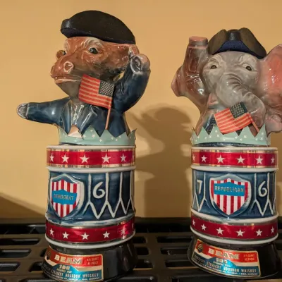 Pair of vintage Jim Beam political decanters featuring a Democrat donkey and Republican elephant atop drum-shaped bases with patriotic...