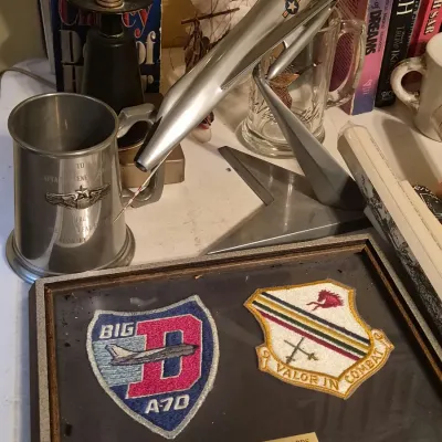 Collection of military memorabilia including framed Air Force patches, a sleek metal airplane model on a stand, and an engraved pewter...