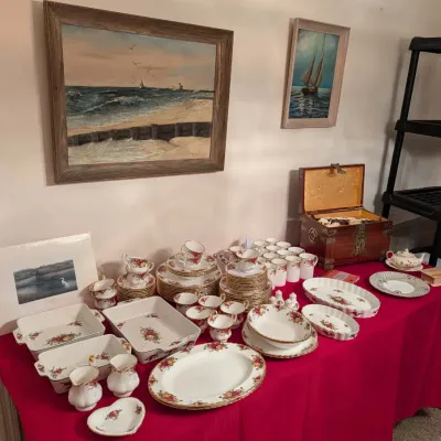 Large collection of Royal Albert Old Country Roses fine bone china tableware displayed alongside framed coastal paintings and a wooden...