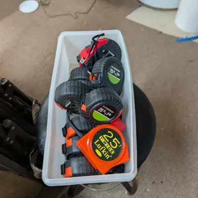 Plastic bin filled with various used tape measures, including Lufkin and Pittsburgh brands.