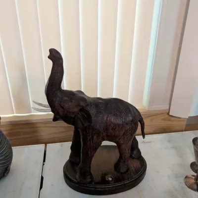 Hand-carved dark wood elephant figurine featuring a raised trunk and white tusks, mounted on an oval wooden base.