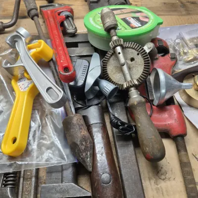 Assortment of vintage hand tools including a hand drill, pipe wrenches, bucket openers, and a soldering iron.