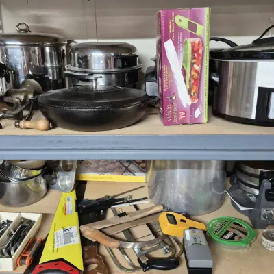 Shelves filled with various kitchenware and household tools, including a Crock-Pot slow cooker, cast iron skillet, stainless steel...
