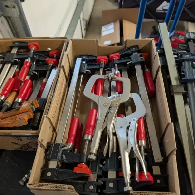 Cardboard boxes filled with woodworking F-clamps with red handles and locking C-clamp pliers.