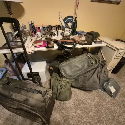 Assortment of military gear and collectibles, including canvas duffel bags, rolling luggage, a holster belt, model airplanes, and books...