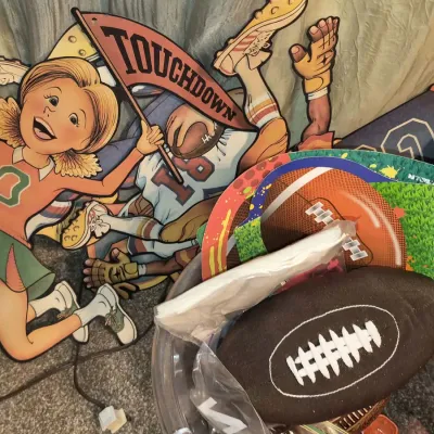 Collection of vintage football-themed decorations, including cardboard cheerleader and player cutouts, a soft plush football, and novelty...