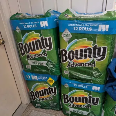 Four unopened 12-roll packages of Bounty Advanced paper towels, stacked on the floor.
