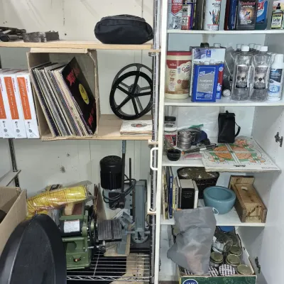 Workshop and storage shelving stocked with vinyl records, benchtop power tools, chemicals, and miscellaneous household items.