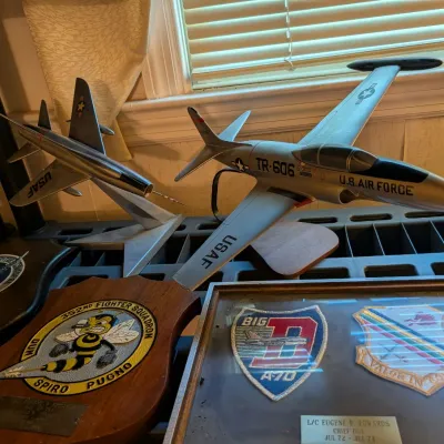 Collection of military memorabilia including U.S. Air Force model jet airplanes on display stands and framed fighter squadron plaques.