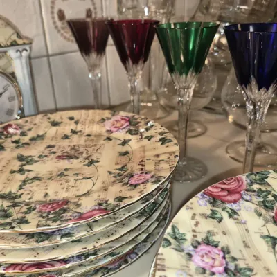 Stack of floral and sheet music patterned porcelain plates displayed with colorful cut-to-clear crystal cordial glasses and a...