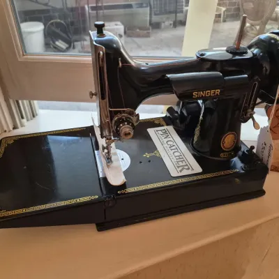 Vintage Singer Featherweight 221 portable sewing machine in black enamel with gold scrollwork trim.