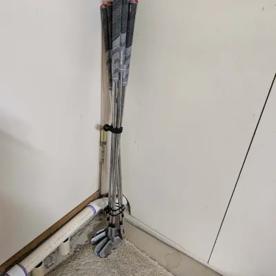Set of golf irons with Golf Pride grips, bundled together with elastic ties in a room corner.