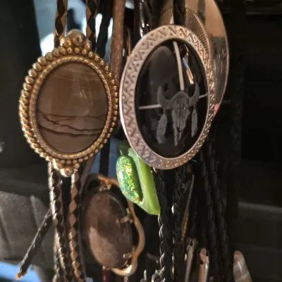 Collection of Western-style bolo ties featuring braided leather cords and decorative slides with stone, resin, and metal designs.