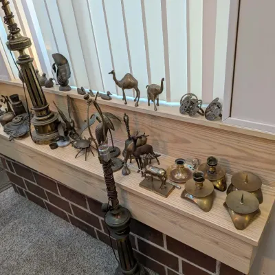 Collection of brass home decor items, including tall column table lamps, candlesticks, and animal figurines arranged on a wooden ledge.