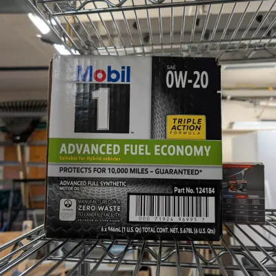 Box of Mobil 1 Advanced Fuel Economy 0W-20 full synthetic motor oil, containing six one-quart bottles, resting on a wire shelf.
