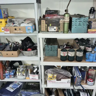 White plastic utility shelving units filled with various workshop items, camping supplies, tools, small propane canisters, and hardware.