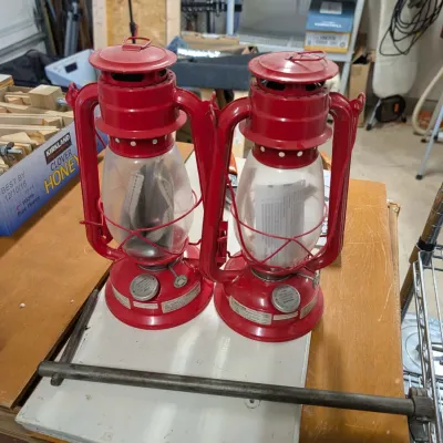 Pair of red vintage-style kerosene lanterns with clear glass globes resting on a wooden tabletop.