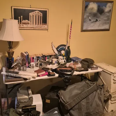 Collection of military memorabilia displayed on a table and floor, including model airplanes, gear bags, leather holster, combat boots,...