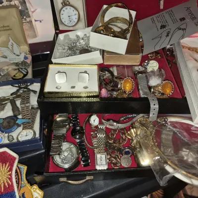 Assortment of vintage jewelry and watches displayed in and around a black jewelry box, including cufflinks, pocket watches, wristwatches,...