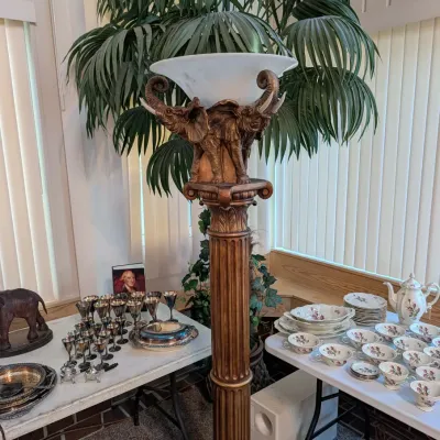 Tall classical fluted pedestal featuring a three-elephant motif top that holds a white frosted glass bowl torchiere light, displayed...