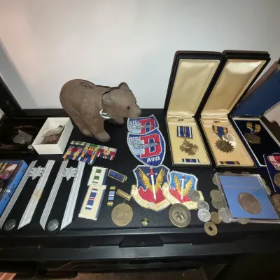 Collection of military memorabilia including boxed medals, ribbon bars, tactical patches, coins, shoulder insignia, and a small bear...