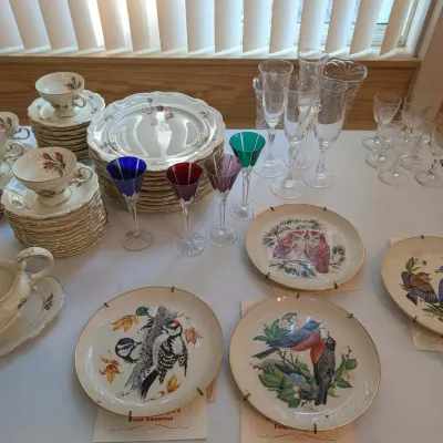 Large collection of tabletop items featuring floral china dishware with gold rims, colored and clear stemware, and a set of decorative...