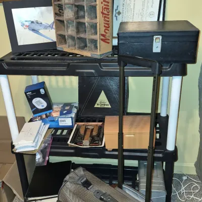 Black plastic shelving unit holding various items, including a vintage Mountain Dew wooden crate, framed military certificate and...