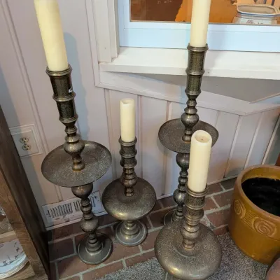 Set of four vintage brass floor-standing candlesticks with ornate etched details and wax pillar candles.