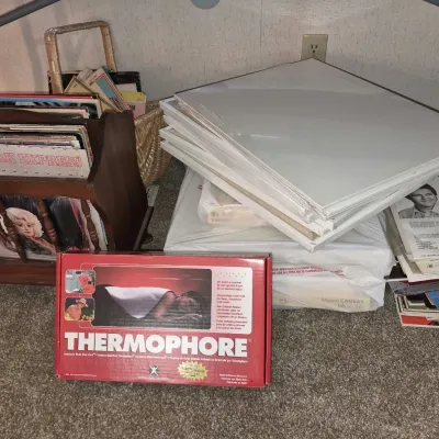 Collection of vinyl LP records in a wooden rack, blank stretched canvases, sheet music, and a vintage Thermophore automatic moist heat...